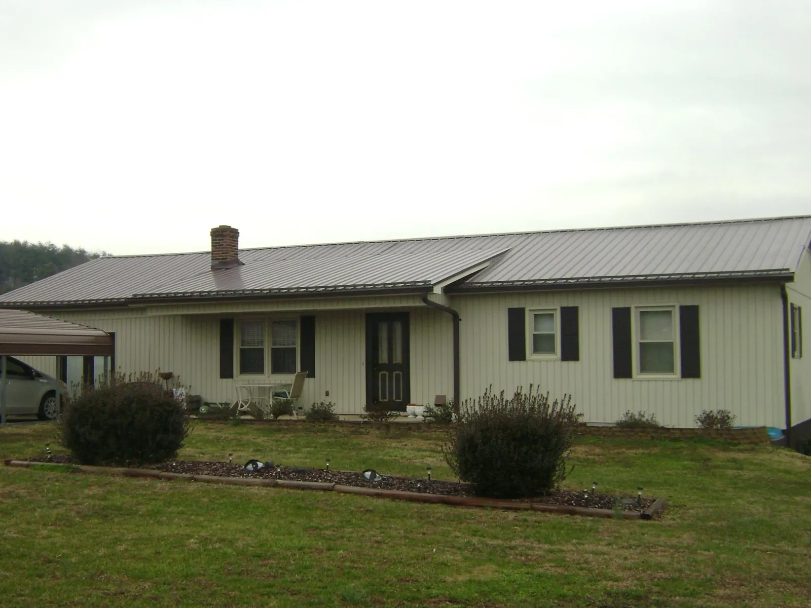 Brown metal roof on a cream sided ranch home with a brick chimney in Fremont